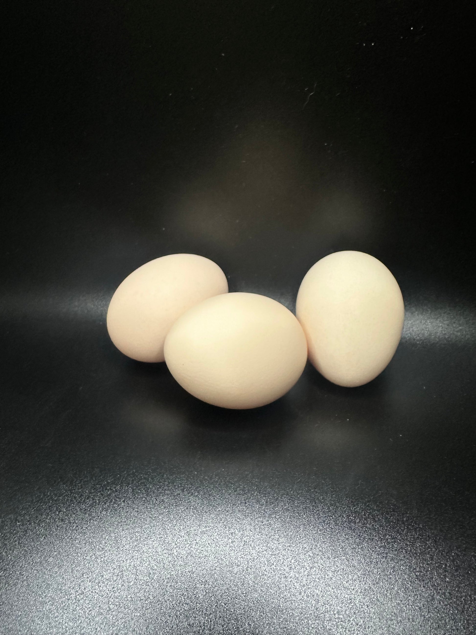 Three white or cream eggs stacked on a black surface